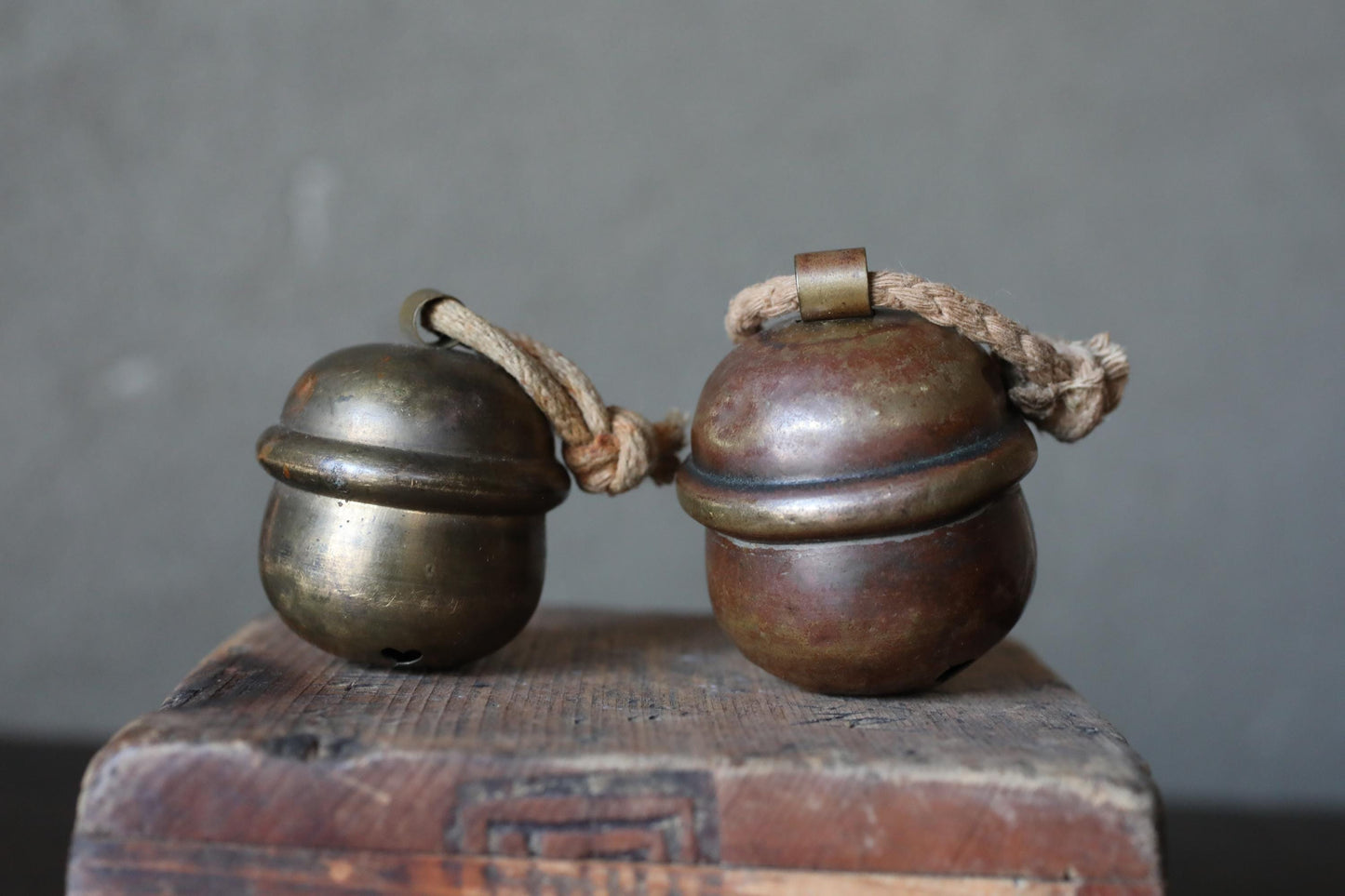Two brass bells with rope handles are placed on a wooden surface.