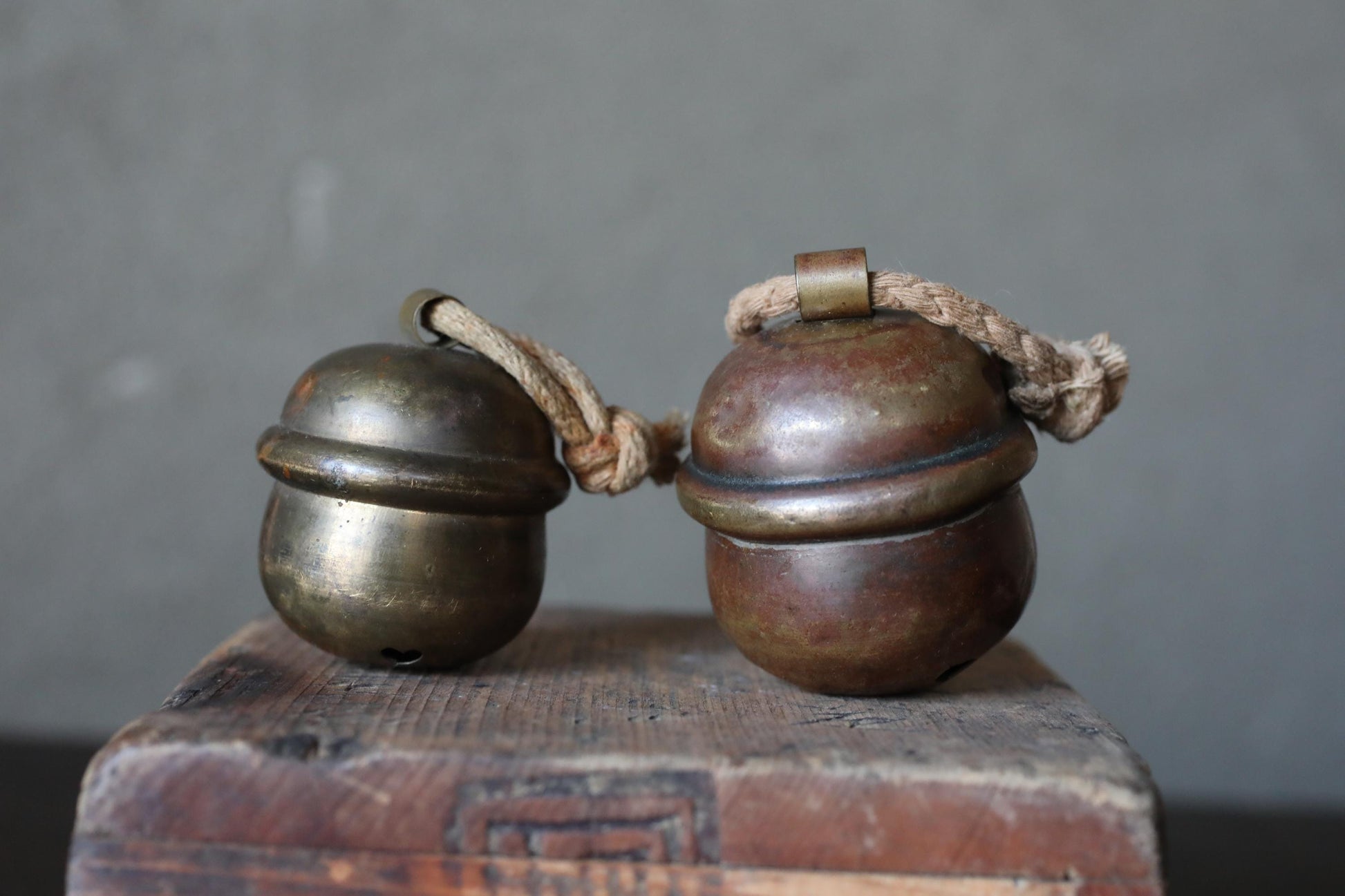 Two brass bells with rope handles are placed on a wooden surface.