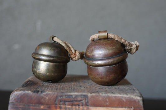 Two brass bells with rope handles are placed on a wooden surface.
