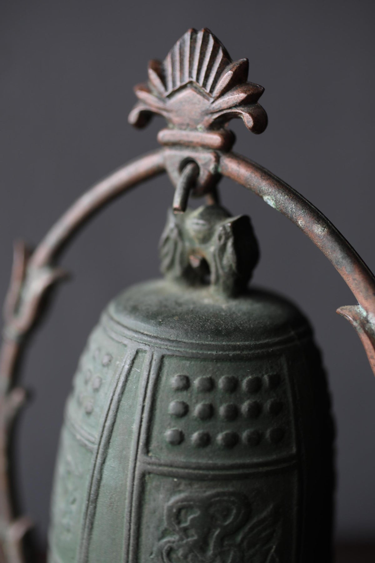 A close-up image of a decorative metal bell with a floral-shaped finial at the top.