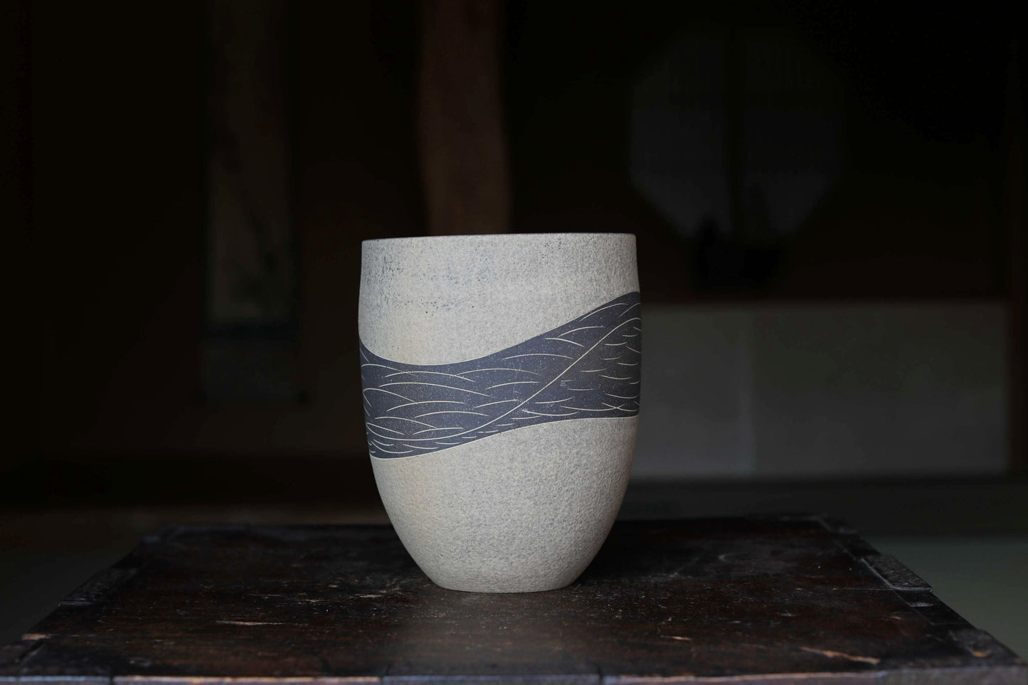 A white ceramic vase with a blue wave pattern on it, placed on a dark wooden surface.