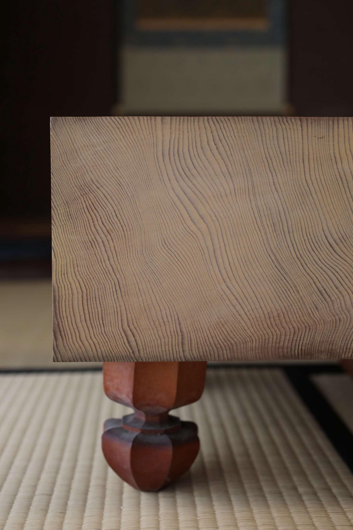 a wooden table with a distinctive, textured finish. The table appears to be made of wood and has a distinctive design, possibly with a natural finish. The table is placed on a mat, which is a common surface for placing items on in a room. The image does not contain any text or other objects, and the focus is solely on the wooden table and its details.