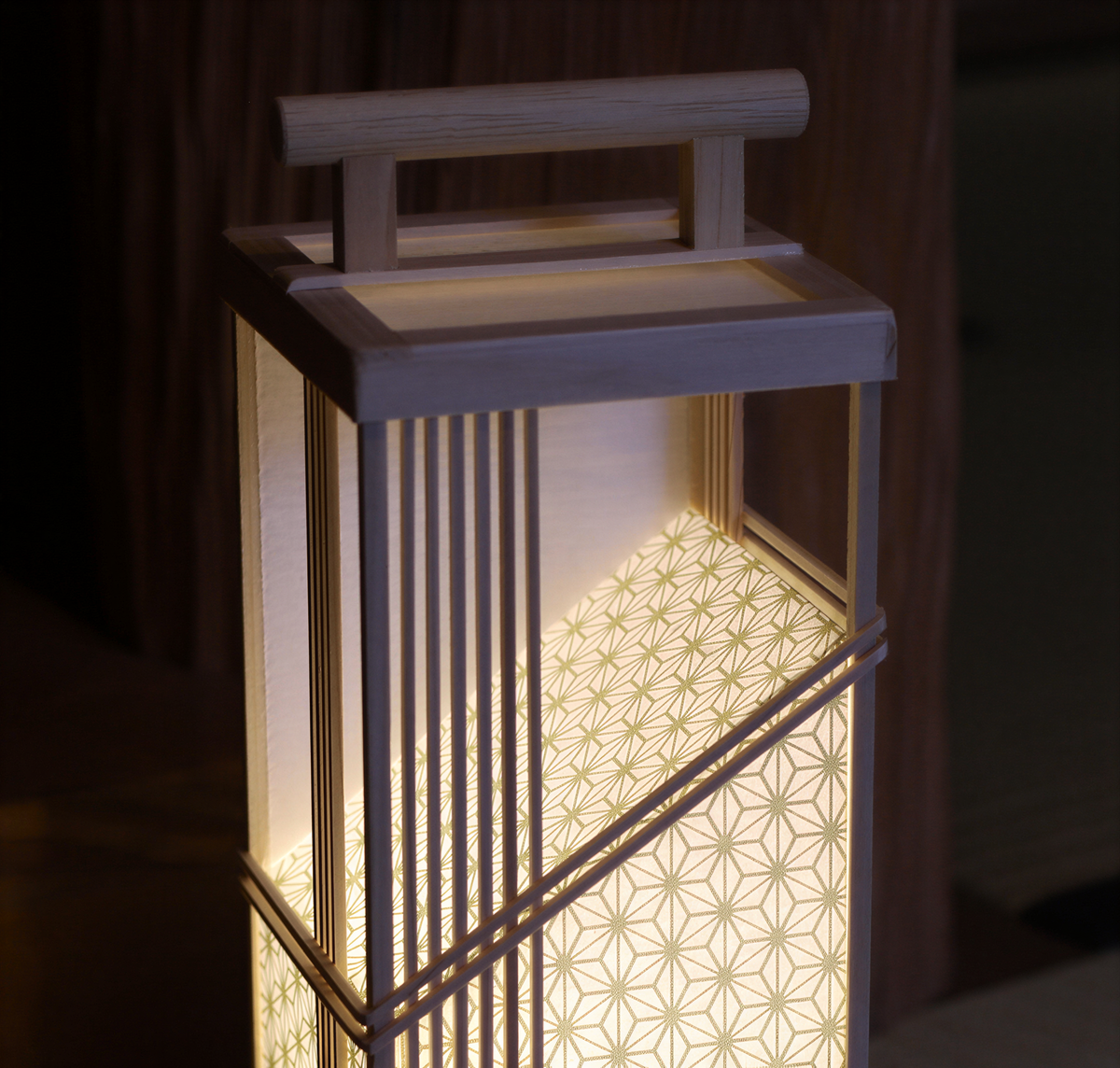 A wooden lantern with a geometric patterned design illuminated by a warm, glowing light.