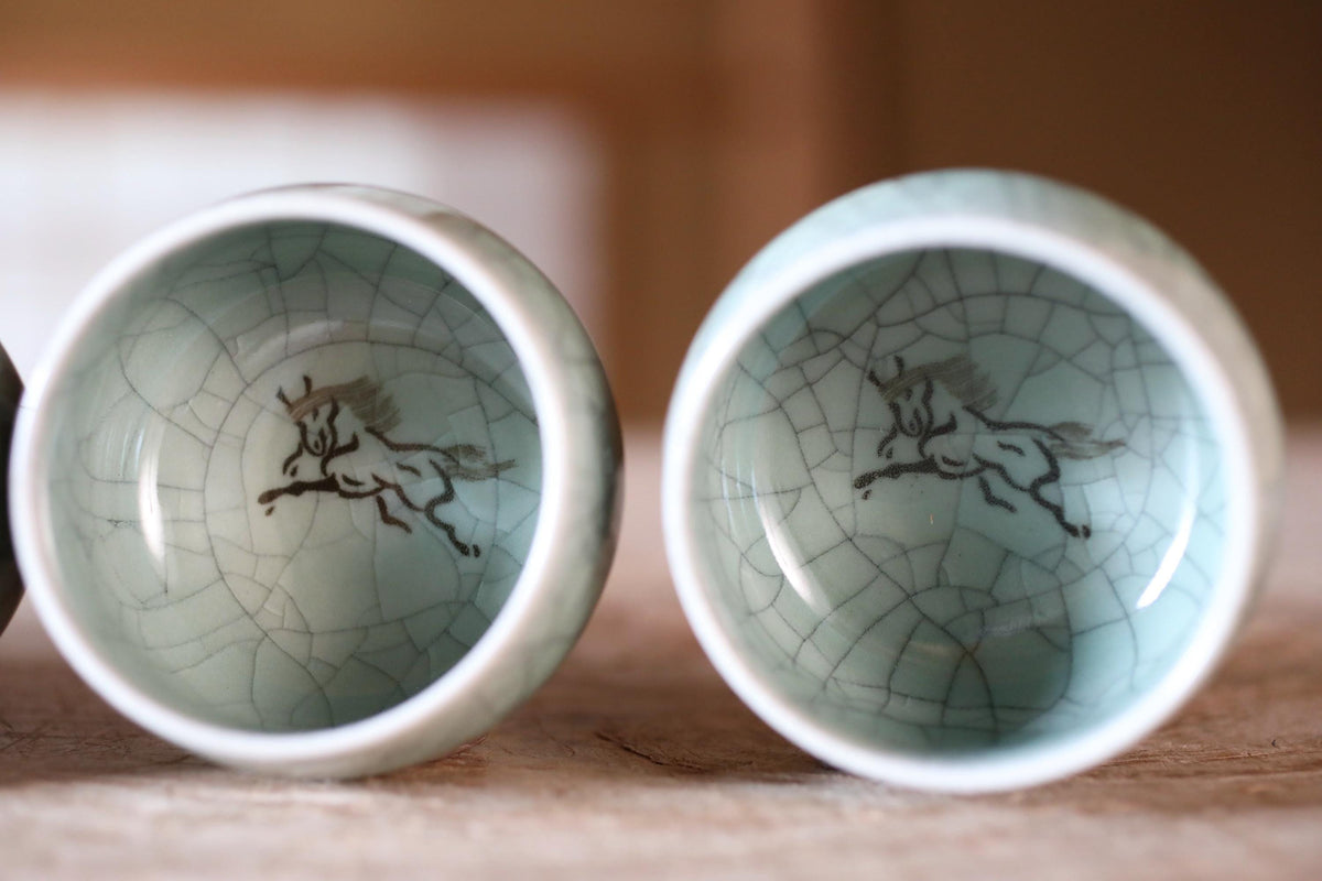 Two ceramic cups with a horse design on them, placed side by side on a wooden surface.