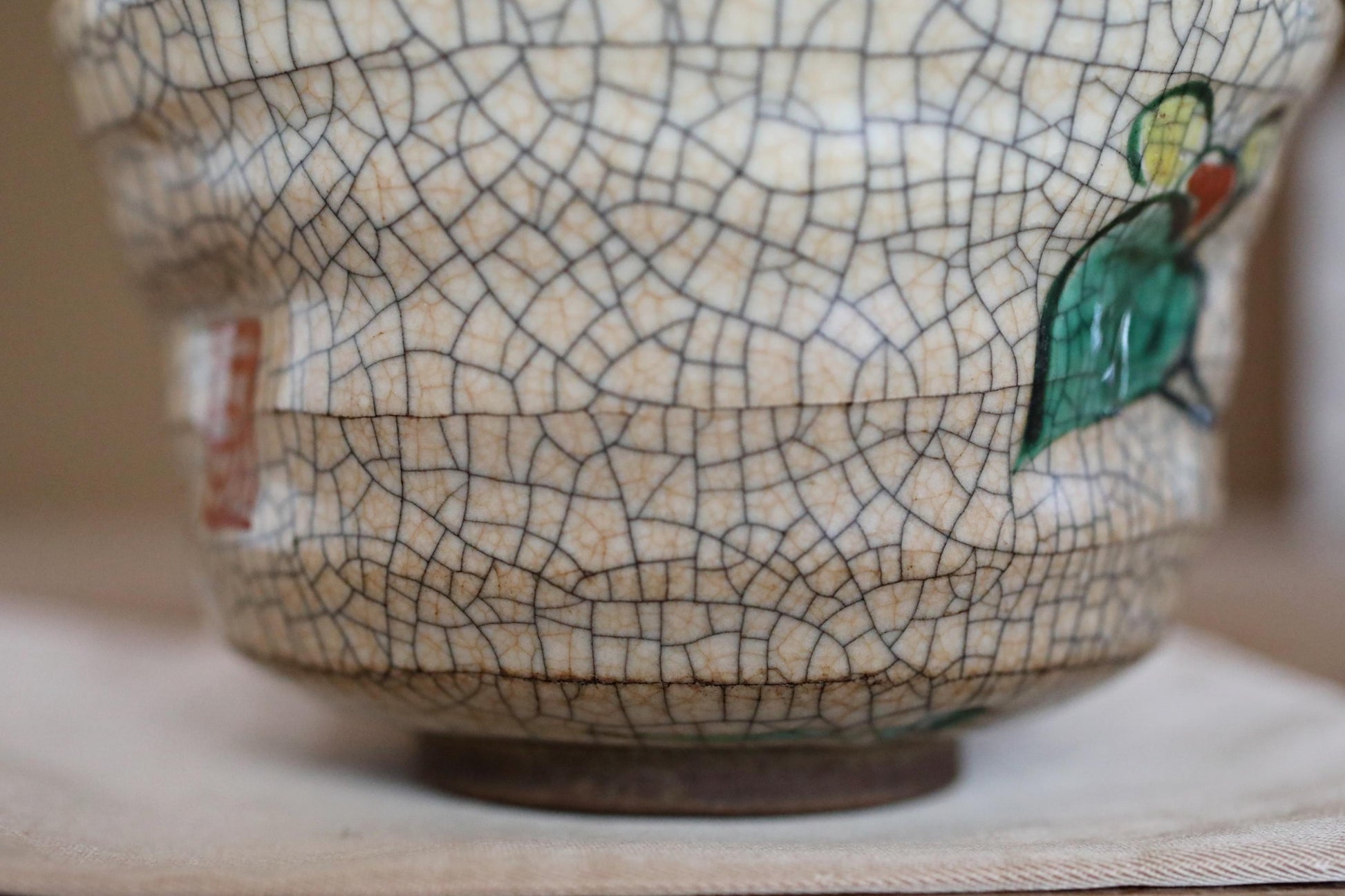 A close-up view of a ceramic vase with a cracked and textured surface, featuring a green leaf design.