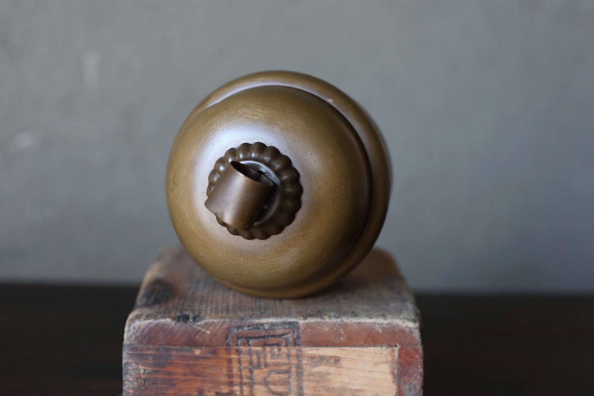 A round, brass-colored object with a small, round finial sits on a wooden surface.